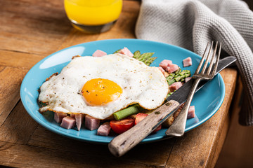 Wall Mural - Healthy breakfast or lunch with fried egg, bread toast, green asparagus and tomatoes on blue plate on old wooden table