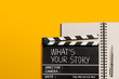 © noppadon - What's your story.Text title on movie clapperboard and notebook on yellow background