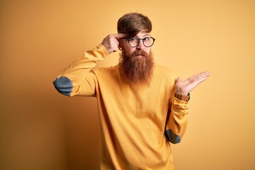 Canvas Print - Handsome Irish redhead man with beard wearing glasses over yellow isolated background confused and annoyed with open palm showing copy space and pointing finger to forehead. Think about it.