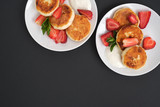 Fototapeta  - Russian and Ukrainian cuisine. Breakfast. Cottage cheese pancakes. Cheesecakes with fresh strawberries, mint and sour cream sauce in a white plate on a light grey background. Copy space mocap top view