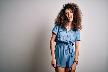 Young beautiful woman with curly hair and piercing wearing casual denim dress winking looking at the camera with sexy expression, cheerful and happy face.