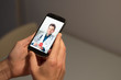 © GENETTICA - Hands holding mobile phone with doctor video call on the screen