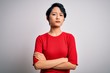 © Krakenimages.com - Young beautiful asian girl wearing casual red t-shirt standing over isolated white background skeptic and nervous, disapproving expression on face with crossed arms. Negative person.