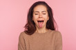 Portrait of funny disobedient young woman with brunette hair keeping eyes closed and demonstrating tongue, behaving naughty unruly, childish mood. indoor studio shot isolated on pink background