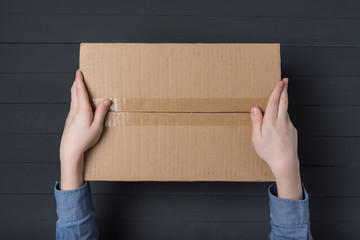 Child hands holding large cardboard box. Delivery of parcels to house. Top view