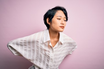 Poster - Young beautiful asian girl wearing casual shirt standing over isolated pink background Suffering of backache, touching back with hand, muscular pain