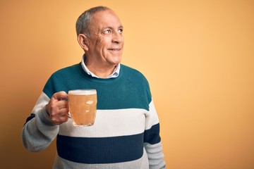 Sticker - Senior handsome man drinking jar of beer standing over isolated yellow background smiling looking to the side and staring away thinking.