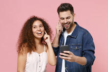 Smiling Young Couple Friends European Guy African American Girl In Casual Clothes Posing Isolated On Pastel Pink Background. People Lifestyle Concept. Listen Music With Earphones Using Mobile Phone.