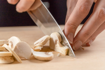 women's hands cut mushrooms on a wooden board close up