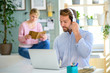 © Halfpoint - Mature businessman with headphones and laptop indoors in home office, working.