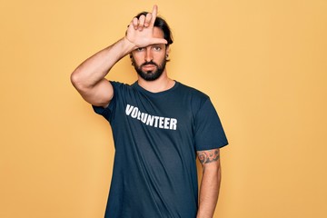 Wall Mural - Young handsome hispanic volunteer man wearing volunteering t-shirt as social care making fun of people with fingers on forehead doing loser gesture mocking and insulting.