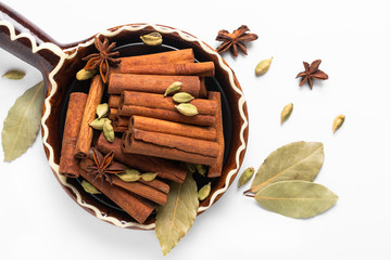 Wall Mural - Healthy food ingredient mix of spices organic Cinnamon sticks, star anise, bay leaves and Cardamom pods in brown handle ceramic bowl on white background