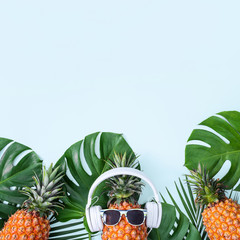 Sticker - Funny pineapple wearing white headphone, concept of listening music, isolated on blue background with tropical palm leaves, top view, flat lay design.