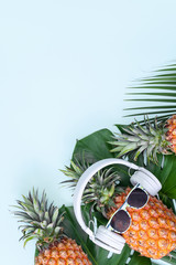 Wall Mural - Funny pineapple wearing white headphone, concept of listening music, isolated on blue background with tropical palm leaves, top view, flat lay design.