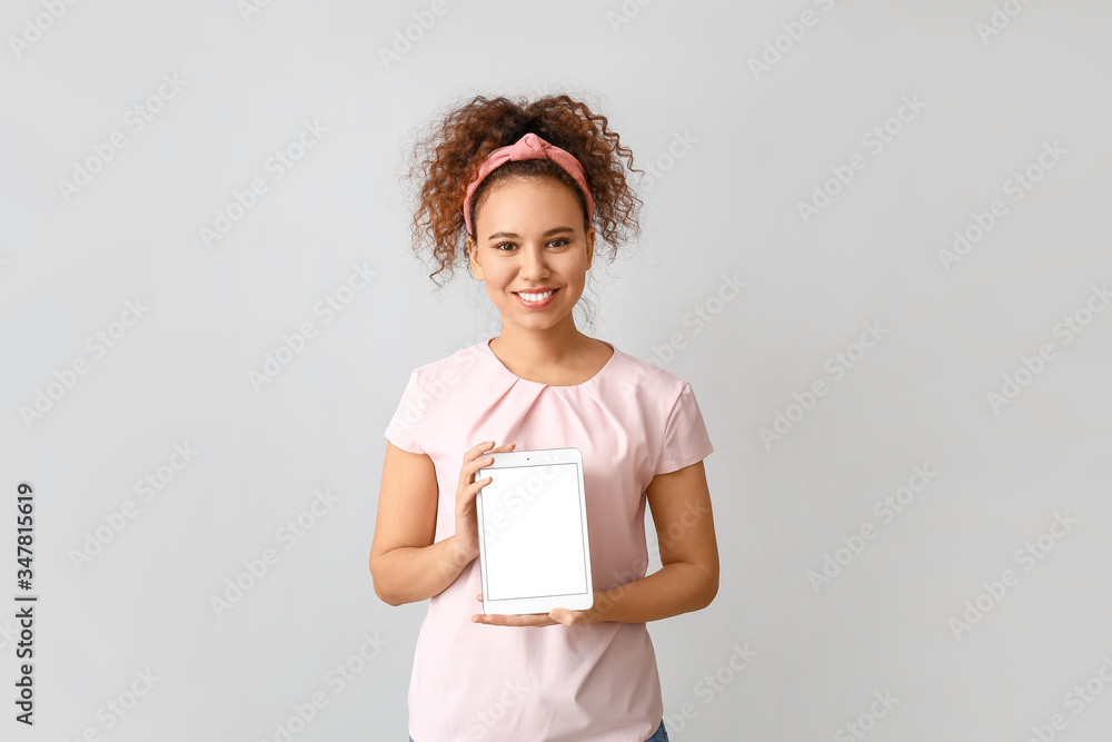 Beautiful young African-American woman with tablet computer on grey background