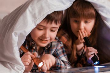 Poster - Little children reading book under blanket at night