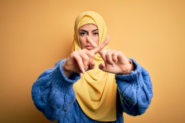 Sticker - Young beautiful brunette muslim woman wearing arab hijab over isolated yellow background Rejection expression crossing fingers doing negative sign