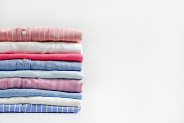 Wall Mural - Stack of colorful perfectly folded clothing items. Pile of different pastel color shirts, sweaters isolated and other garments on white background. Close up, copy space.