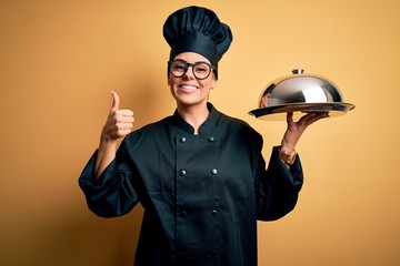 Poster - Young beautiful brunette chefwoman wearing cooker uniform and hat holding tray with dome happy with big smile doing ok sign, thumb up with fingers, excellent sign