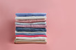 © Evrymmnt - Stack of colorful perfectly folded clothing items. Pile of different pastel color shirts and sweaters isolated on pale pink background. Close up, copy space.