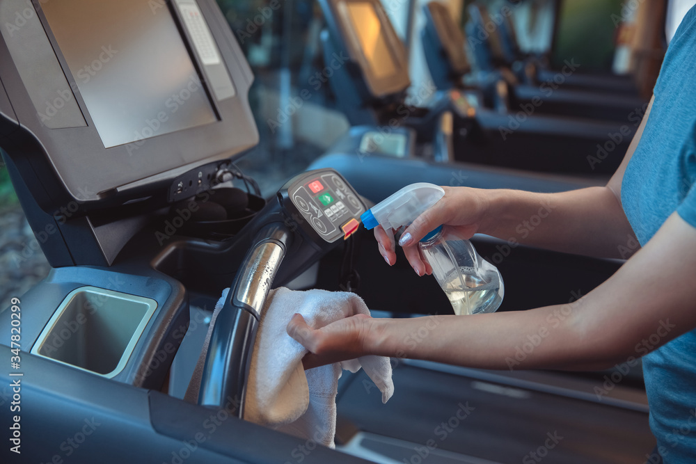 Gym cleaning and disinfection. Infection prevention and control of epidemic. Staff using wipe and alcohol sanitizer spray to clean treadmill in gym. Anti Covid-19 precautions - obrazy, fototapety, plakaty 