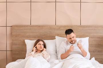 Canvas Print - Young woman cannot sleep because of her husband playing game on mobile phone in bedroom