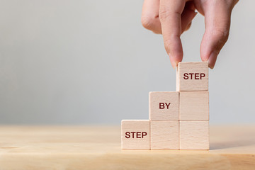 hand arranging wood block stacking as step stair on top with word step by step. business concept for