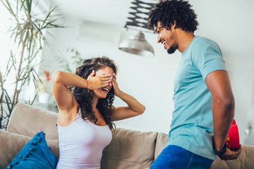 Wall Mural - Smiling man surprises his girlfriend with present at home.