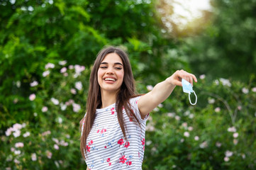 Woman throwing away her mask. young happy girl looking at protective medical mask, take off remove mask from her face. End of pandemic coronavirus concept. NCoV, Covid 19. Pollen allergy at spring