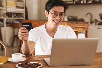 Sticker - Image of smiling asian man holding credit card while using laptop