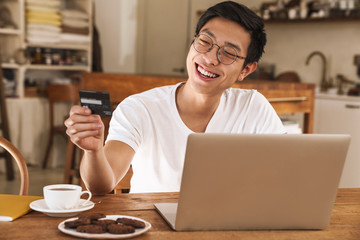 Poster - Image of asian man winking while holding credit card and using laptop