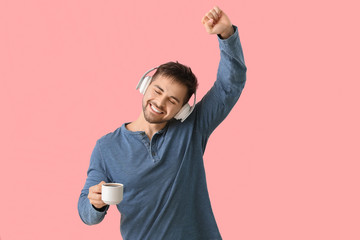 Canvas Print - Young man with cup of hot coffee listening to music on color background