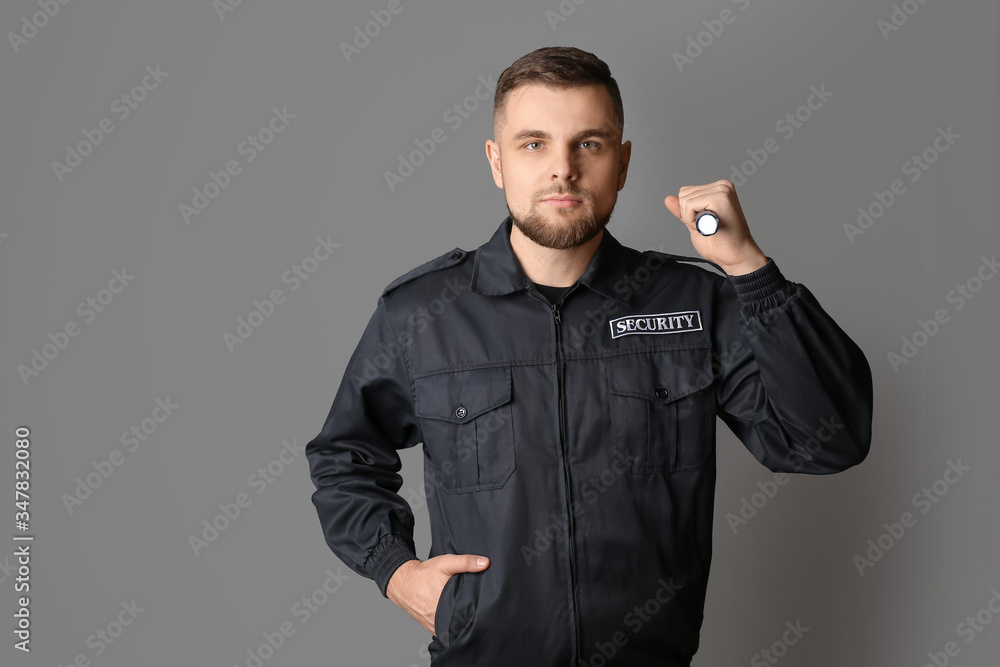 Male security guard with flashlight on grey background