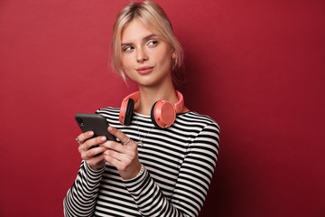 Wall Mural - Image of nice thinking woman with headphones typing on cellphone