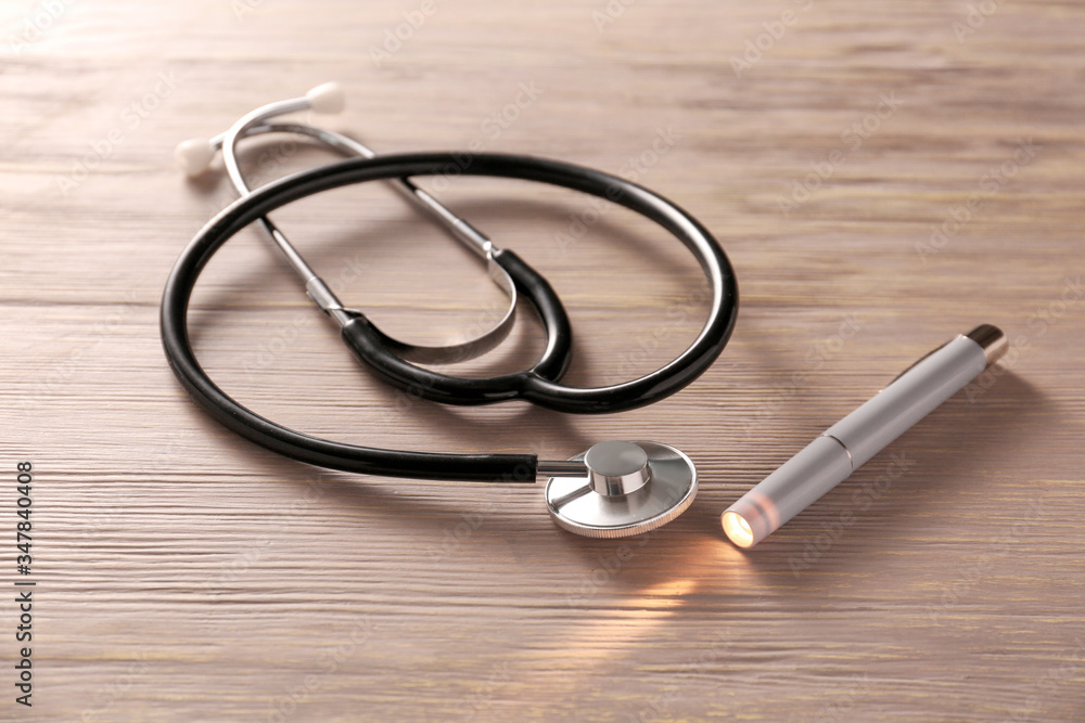 Modern flashlight with stethoscope on wooden background