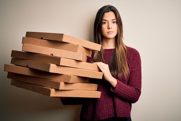 Poster - Young beautiful girl holding delivery Italian pizza boxes standing over white background with a confident expression on smart face thinking serious