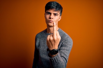 Poster - Young handsome man wearing casual sweater standing over isolated orange background Showing middle finger, impolite and rude fuck off expression