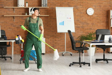 Canvas Print - Male janitor listening to music while mopping floor in office