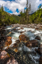 A Mountain River With A Rocky Bottom Flowing Among The Forest. Big Wet Stones. Far Away Are Mountains And Low White Clouds. Vertical.