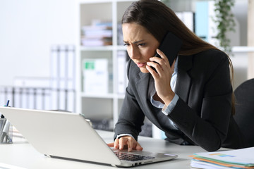 worried executive calling on phone checking laptop at office