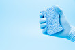 © Kenishirotie - Hand in blue glove with sponge isolated on blue background for cleaning
