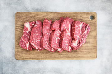 Fresh raw beef steaks on wooden cutting board on gray background. Copy space, top view.