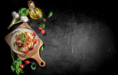 Wall Mural - Heaped plate of delicious Italian spaghetti pasta with fresh basil leaves and grated parmesan cheese on dark background