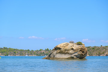 Rock in middle of the blue water like a small island with green hill in the background