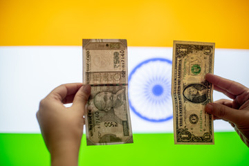 Hands holding an american dollar of united states of america and indian rupee in front of an indian flag comparing the value while it fluctuates