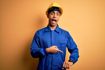 Young handsome african american worker man wearing blue uniform and security helmet In hurry pointing to watch time, impatience, upset and angry for deadline delay