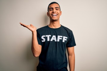 Young handsome african american worker man wearing staff uniform over white background smiling cheerful presenting and pointing with palm of hand looking at the camera.