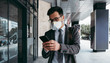© Cavan Images - Business man with protective face mask using phone on city street.