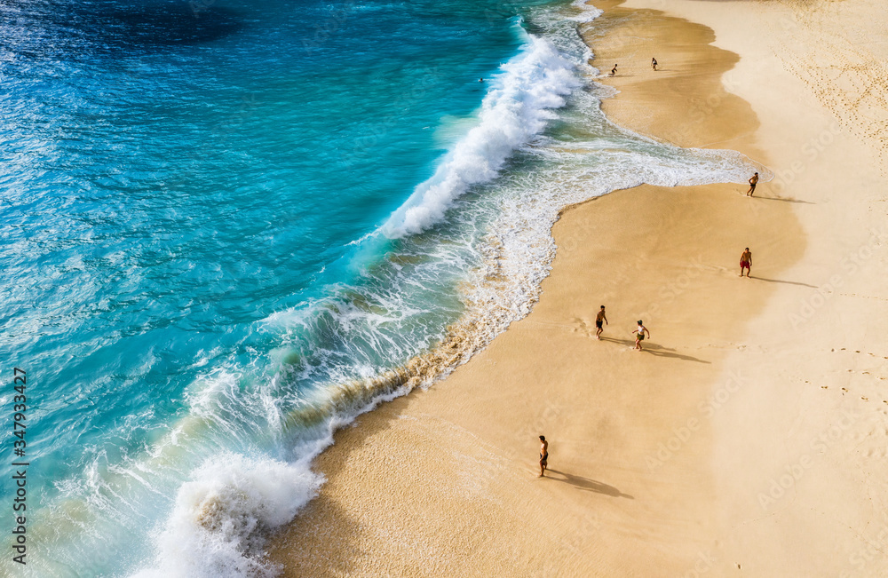People on the beach on Bali, Indonesia. Vacation and adventure. Beach and large waves. Top view from drone at beach, azure sea and relax people. Travel and relax - image - obrazy, fototapety, plakaty 