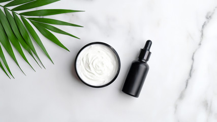 Wall Mural - a close up of black aromatic oil bottle and hand cream on marble background with palm leaves.